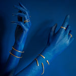 model with blue hand on blue background wearing brass rings and cuffs