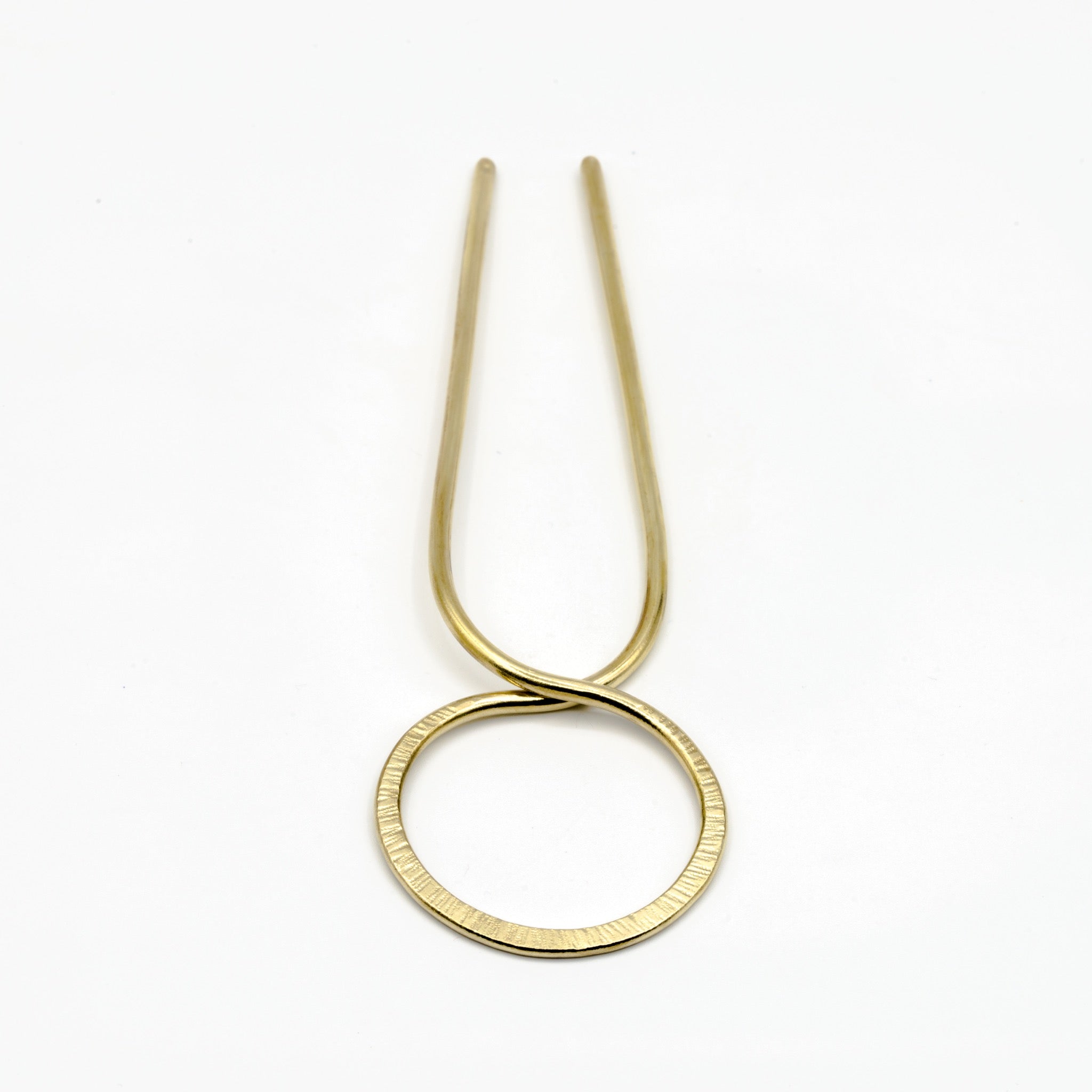 close up of brass hair pin with striped texture on white background