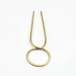 close up of brass hair pin with striped texture on white background
