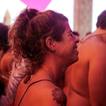 Mulher com uma tatuagem no braço numa multidão com iluminação acolhedora, usando brincos de prata