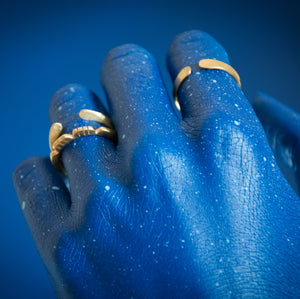 mão pintada de azul sobre fundo azul com anéis de latão