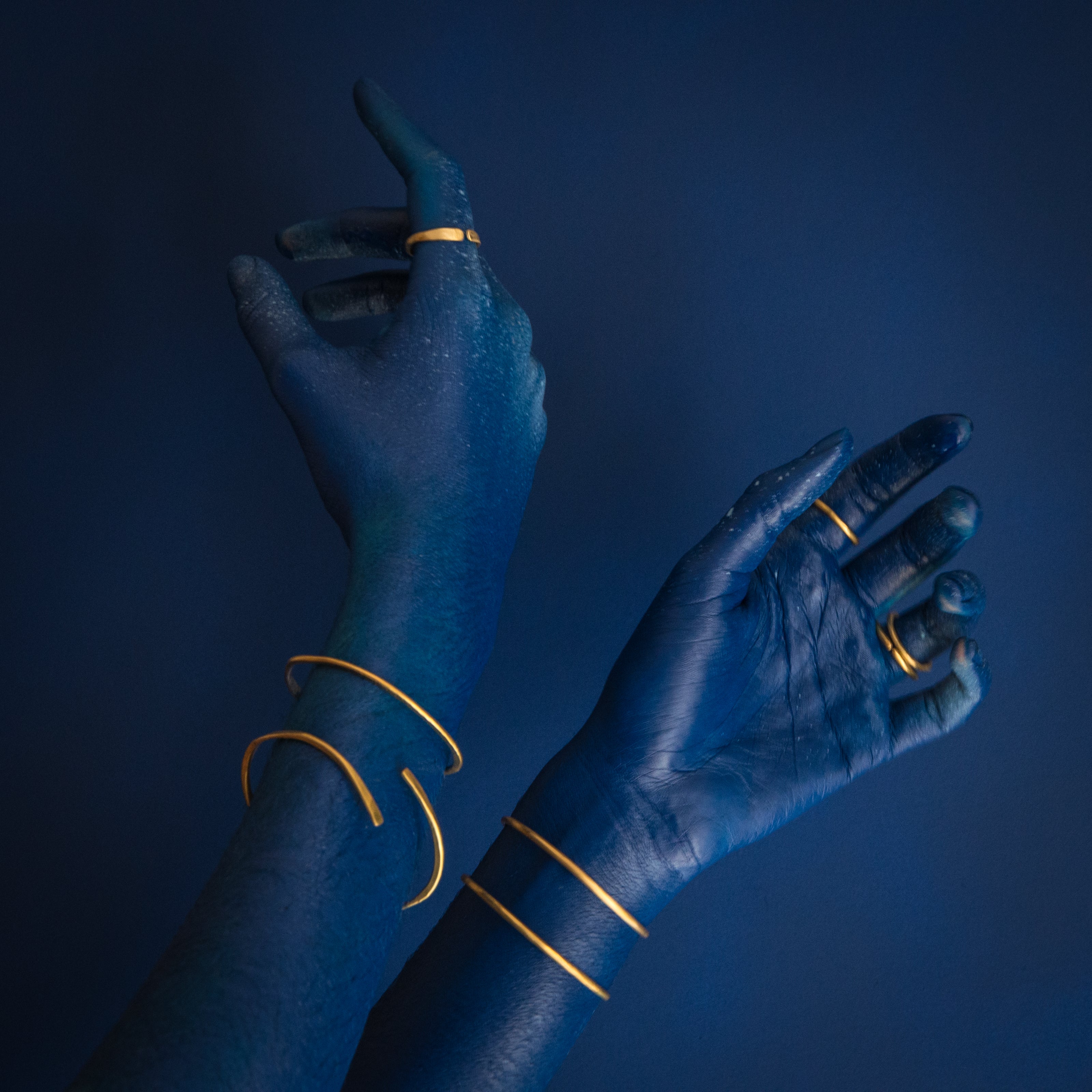 mãos azuis sobre fundo azul usando anéis de latão e pulseiras