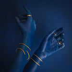 mãos azuis sobre fundo azul usando anéis de latão e pulseiras