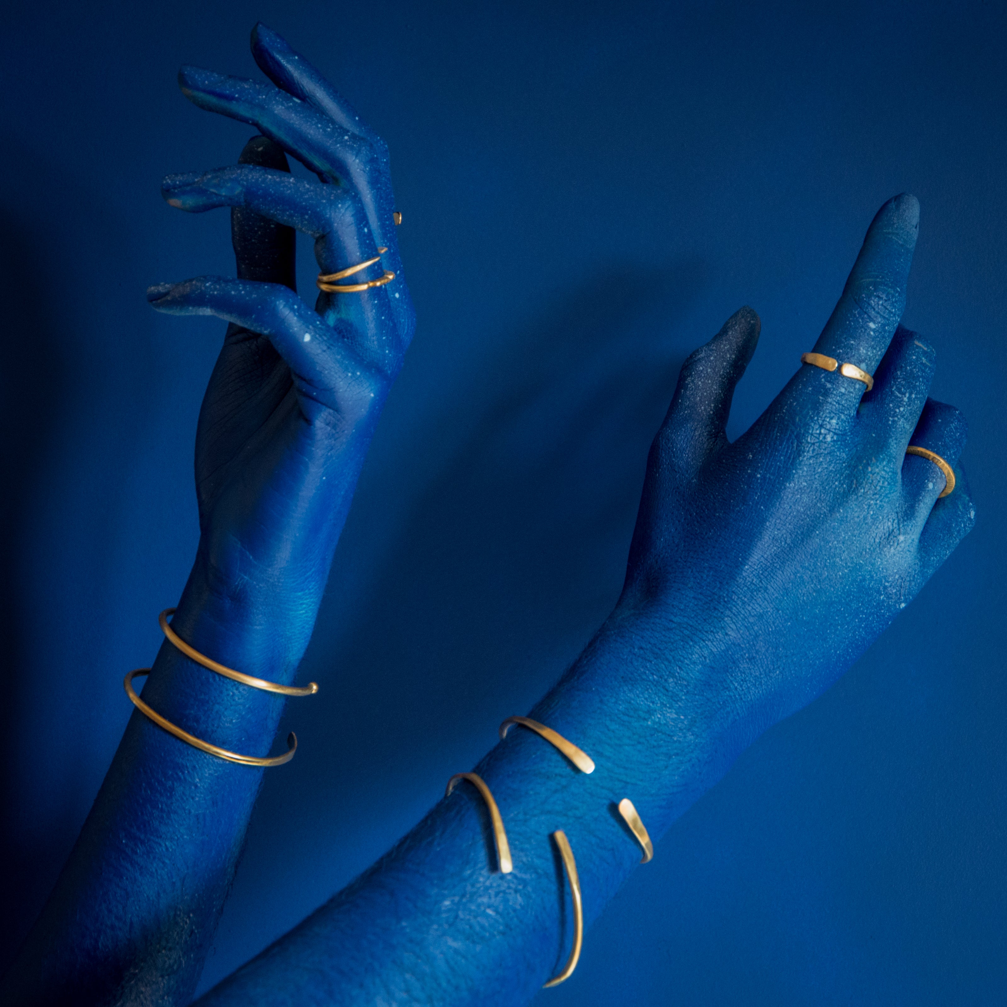 modelo com mão azul sobre fundo azul usando anéis de latão e pulseiras