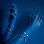 modelo com mão azul sobre fundo azul usando anéis de latão e pulseiras