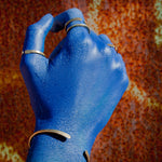 mão pintada de azul com anéis de latão sobre fundo enferrujado