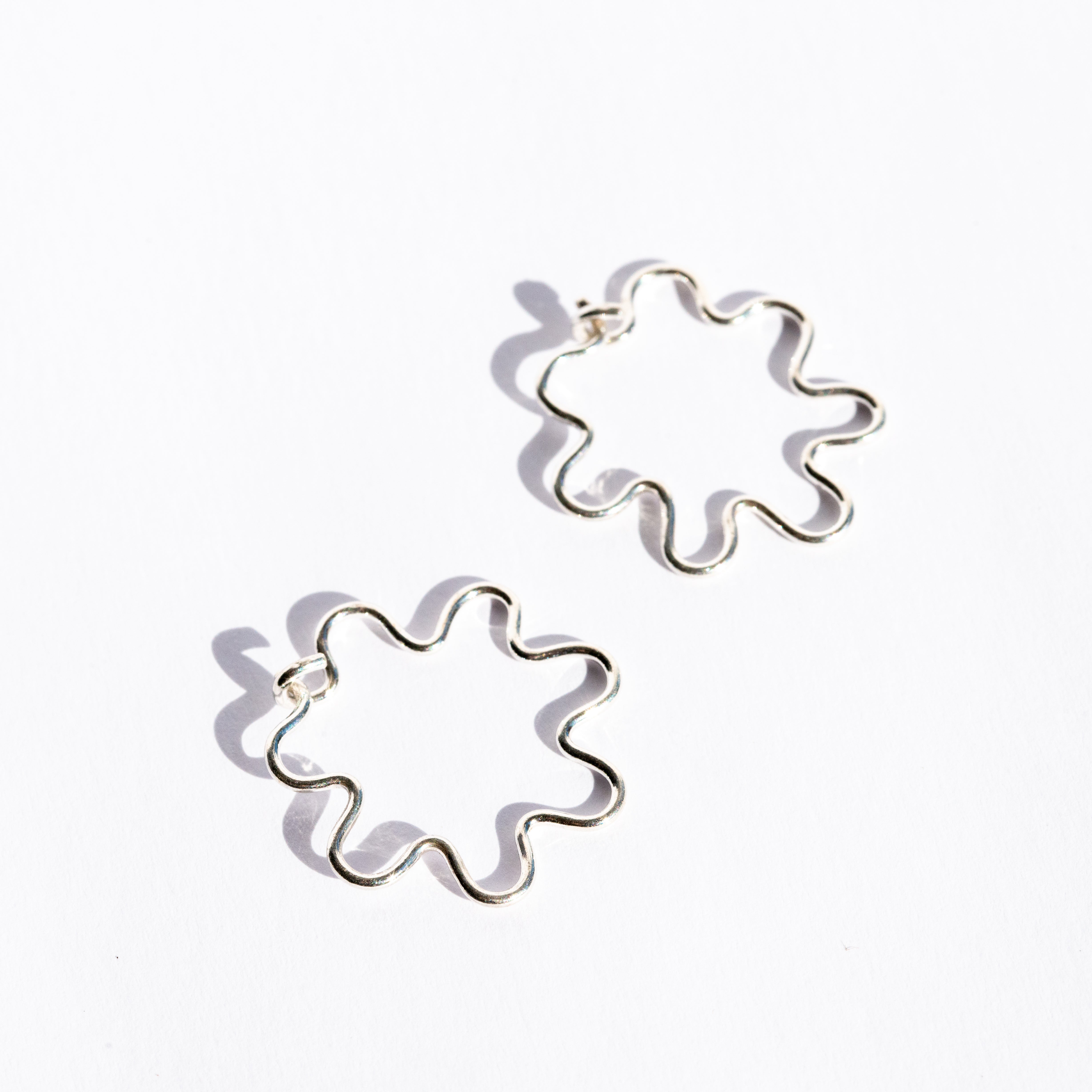Pair of silver wavy flower-shaped earrings on a white background