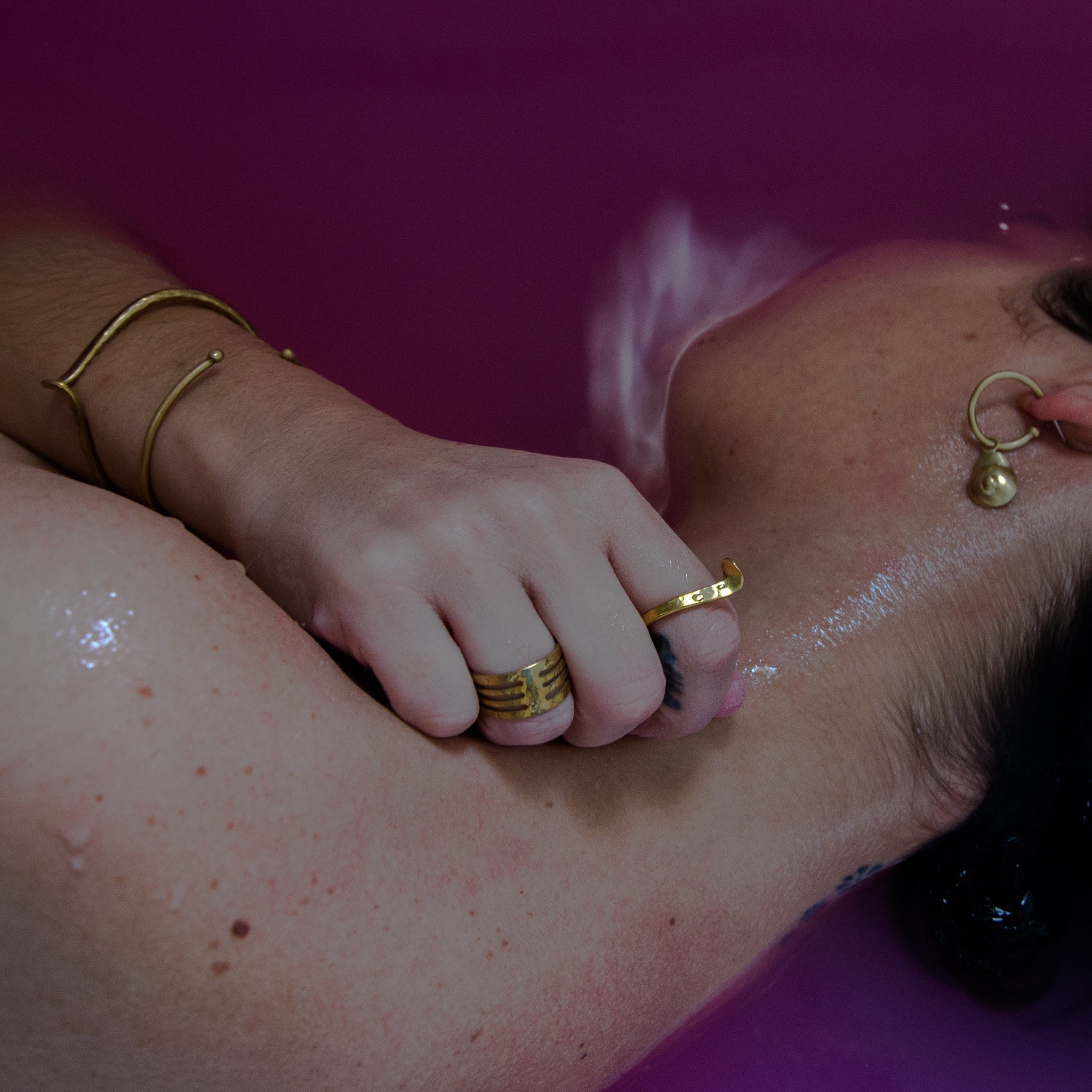 model in pink water wearing brass jewelry