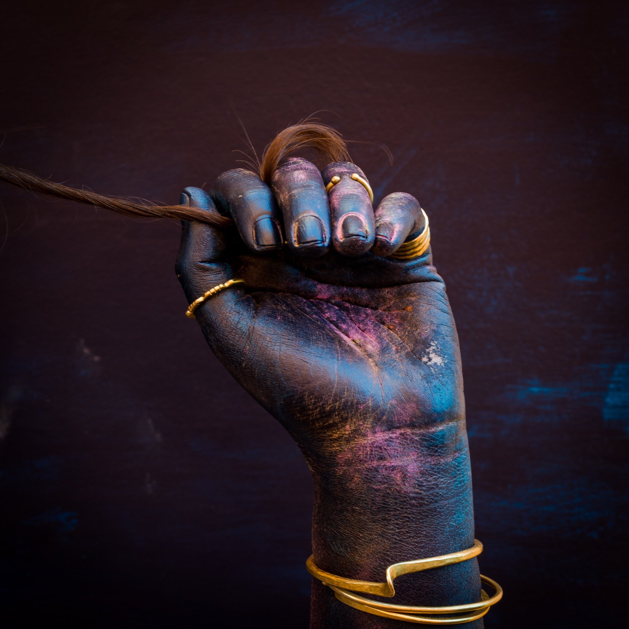 blue painted hand holding hair with brass rings and bracelets