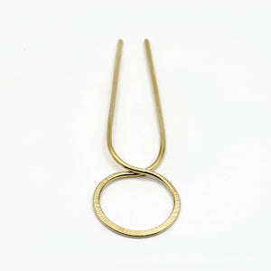 close up of brass hair pin with striped texture on white background