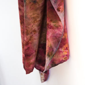 side view of hanging silk scarf. oranges, red and pinks cover the fabric
