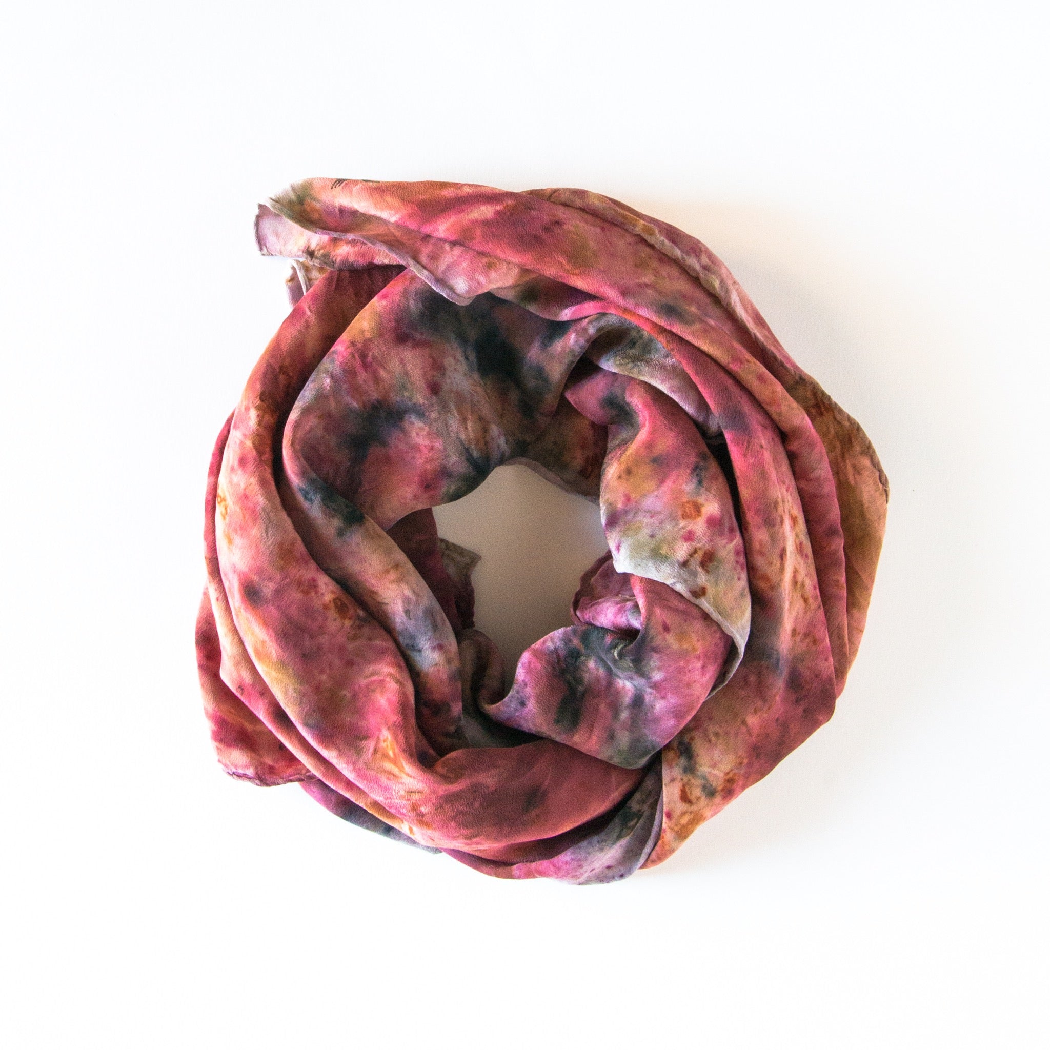 top view of rolled scarf on white background. pinks, oranges and dark purples