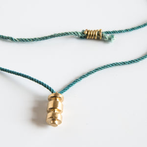 Sculpted brass pendant on this green silk rope close up
