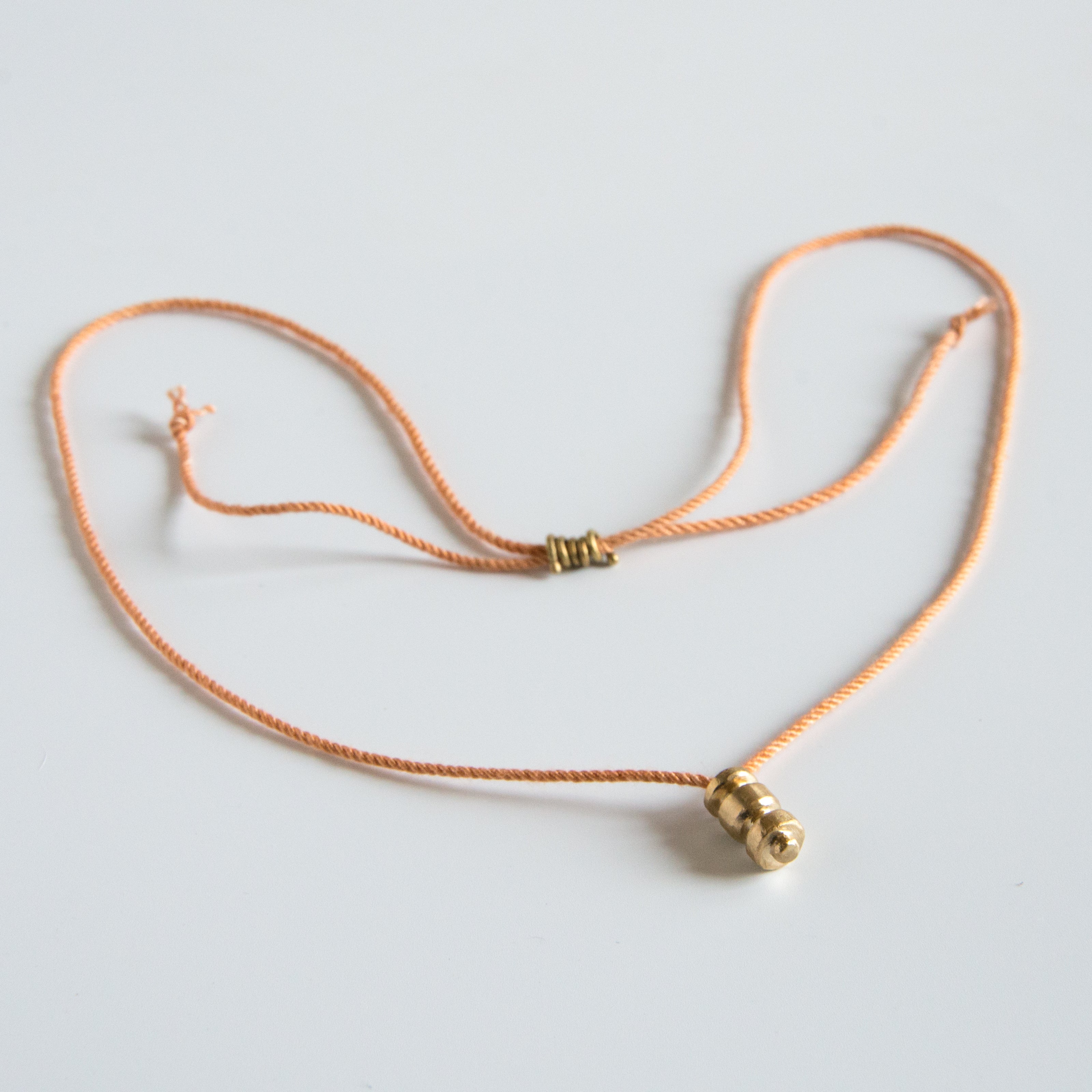 Sculpted brass pendant on this orange silk rope