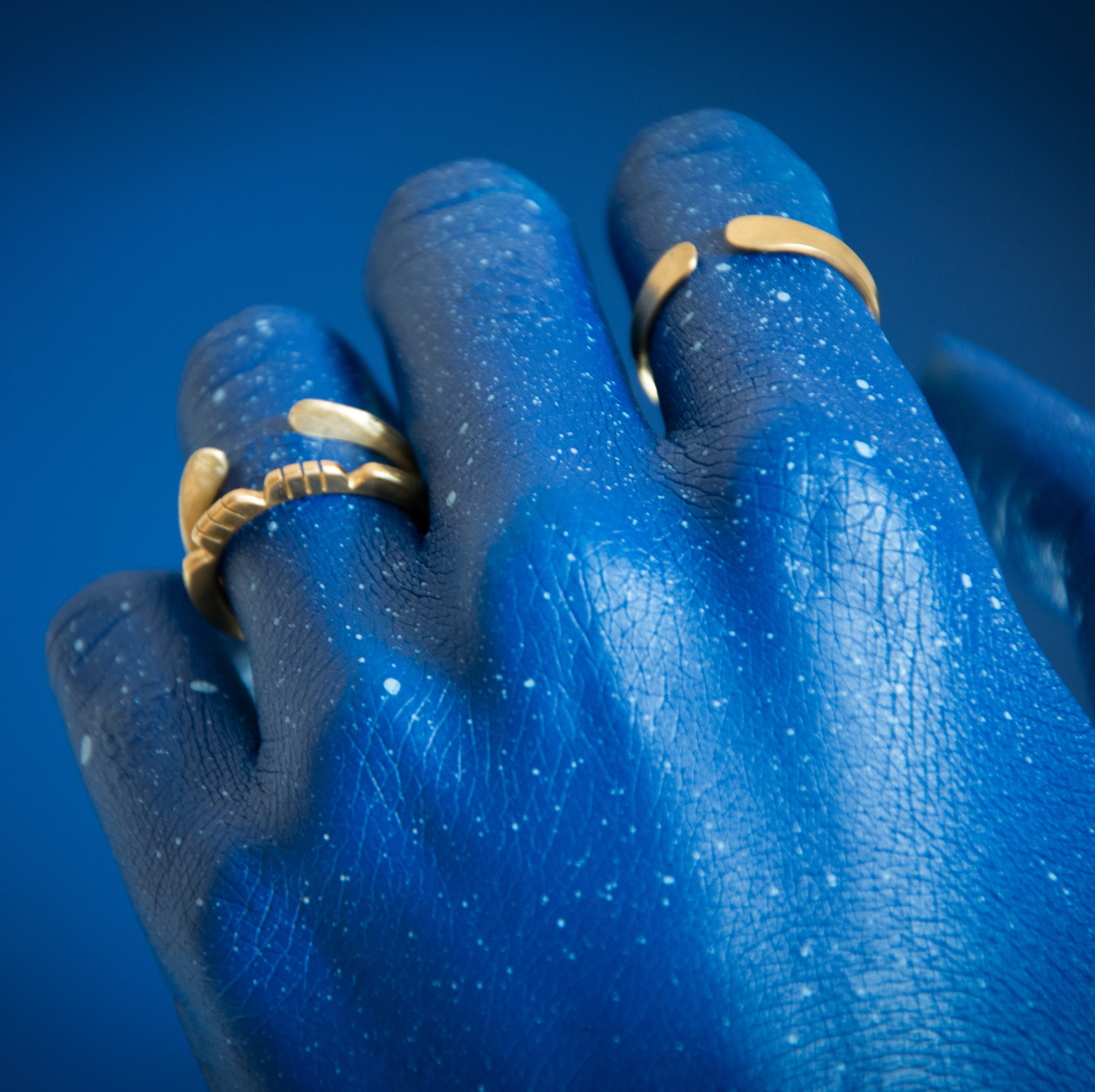 model painted blue in blue background wearing brass rings